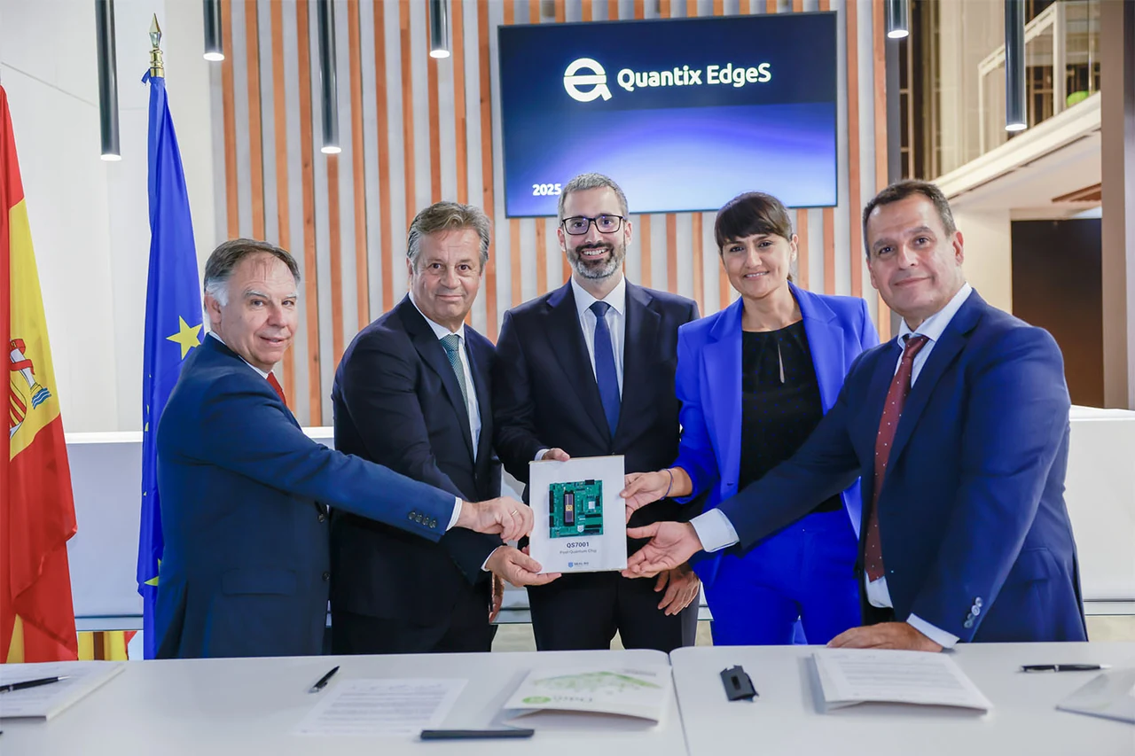 Five signatories holding a framed QS7001 post-quantum chip in front of a Quantix EdgeS screen, with the Spanish and European flags behind them.